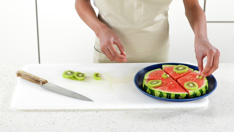 Fordel kiwiskivene på vannmelonen. Du kan også skjære noen av kiwiskivene i mindre biter. Blir det noen skiver til overs, kan du kose deg med disse mens du lager ferdig pizzaen.