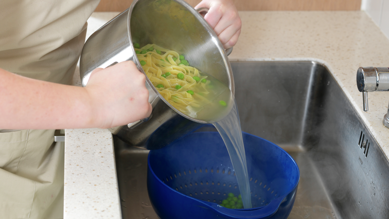 Sett et dørslag på en tallerken i vasken. Hell pastaen og ertene i dørslaget. Løft det opp og rist litt slik at alt vannet renner av.
