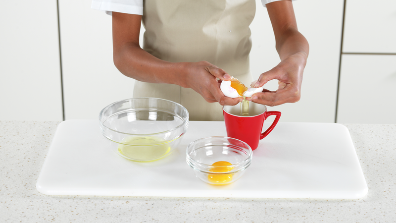 Nå skal du skille egg, fordi du kun skal bruke eggeplommene. Finn frem en kopp og to skåler. Start med et egg og knekk det over koppen.