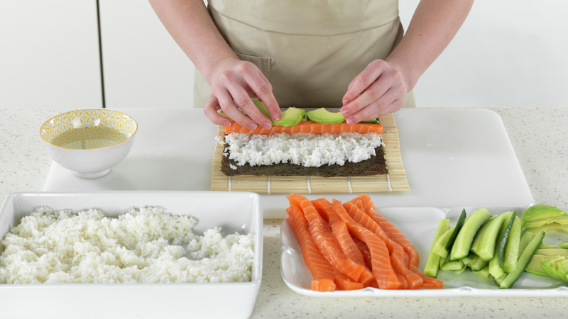 Legg strimler av laks, avokado og agurk ved siden av hverandre på risen.