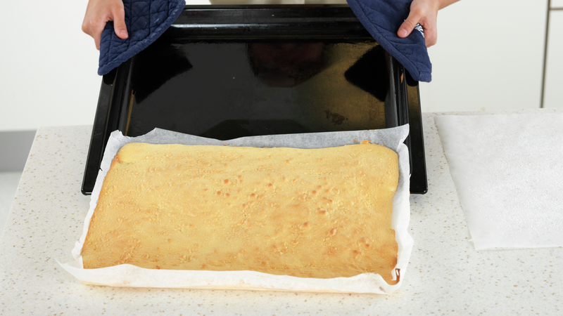 Når kaken er ferdig: Bruk grytekluter og løft langpannen ut av ovnen og la kaken, med bakepapiret, skli av brettet og ned på benken.