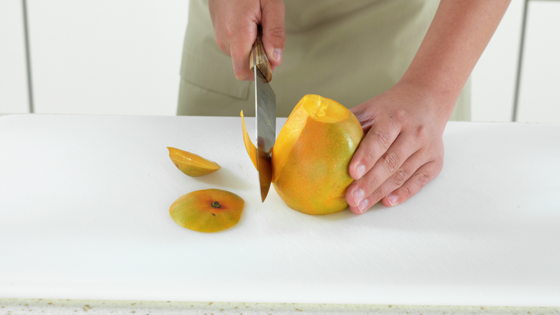 Plasser mangoen stødig på skjærefjølen, med bunnen ned. Skjær av skallet, ved å la kniven gli langs sidene. Prøv å skjær så nærme skallet du klarer, slik at minst mulig havner i søpla.