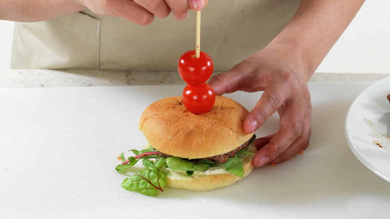 Pynt gjerne burgerne med trespyd og cherrytomat: tre cherrytomat på trespydene og press ned i burgeren. Her kan du godt bruke tomater med ulike farger, hvis du vil.