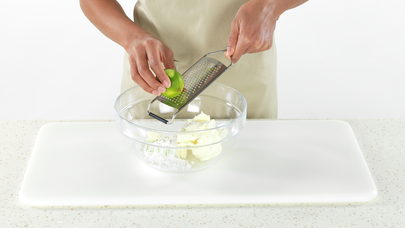 Nå skal du rive skall av lime: Vask limen godt. Bruk et rivjern å rive den mengden limeskall du trenger, og ha i bollen. Riv kun den grønne delen, da den hvite delen smaker bittert. Limen er med på å gi en frisk farge til desserten:).