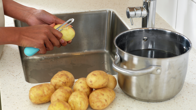 Fyll en stor kjele halvfull med vann. Skyll og skrell potetene over vasken og legg dem i kjelen med vann. Husk å kaste skallet i søpla når du er ferdig.