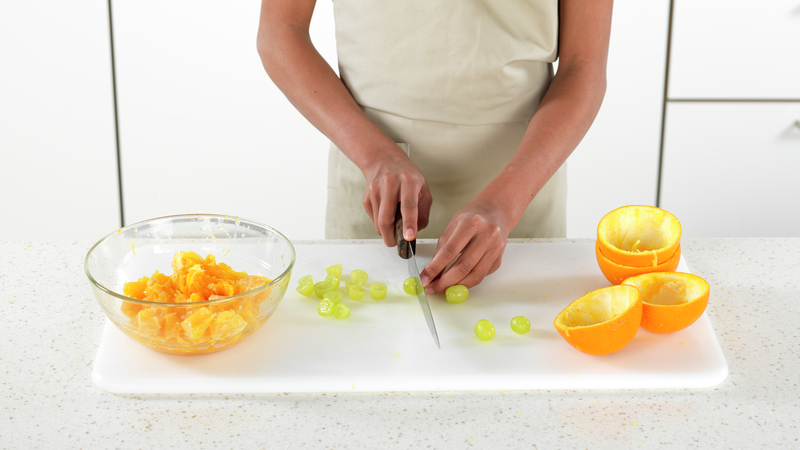 Tørk over fjølen. Del druer i to og ha dem i skålen sammen med appelsinbitene.