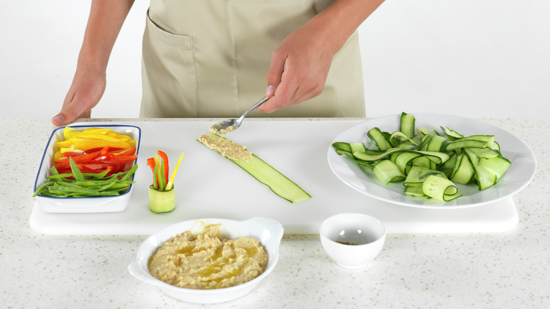 Finn frem alle grønnsakene du har forberedet, hummus og spisskummin (så har du alt klart). Start med å smøre litt hummus på den nedre delen av en agurkstrimel.